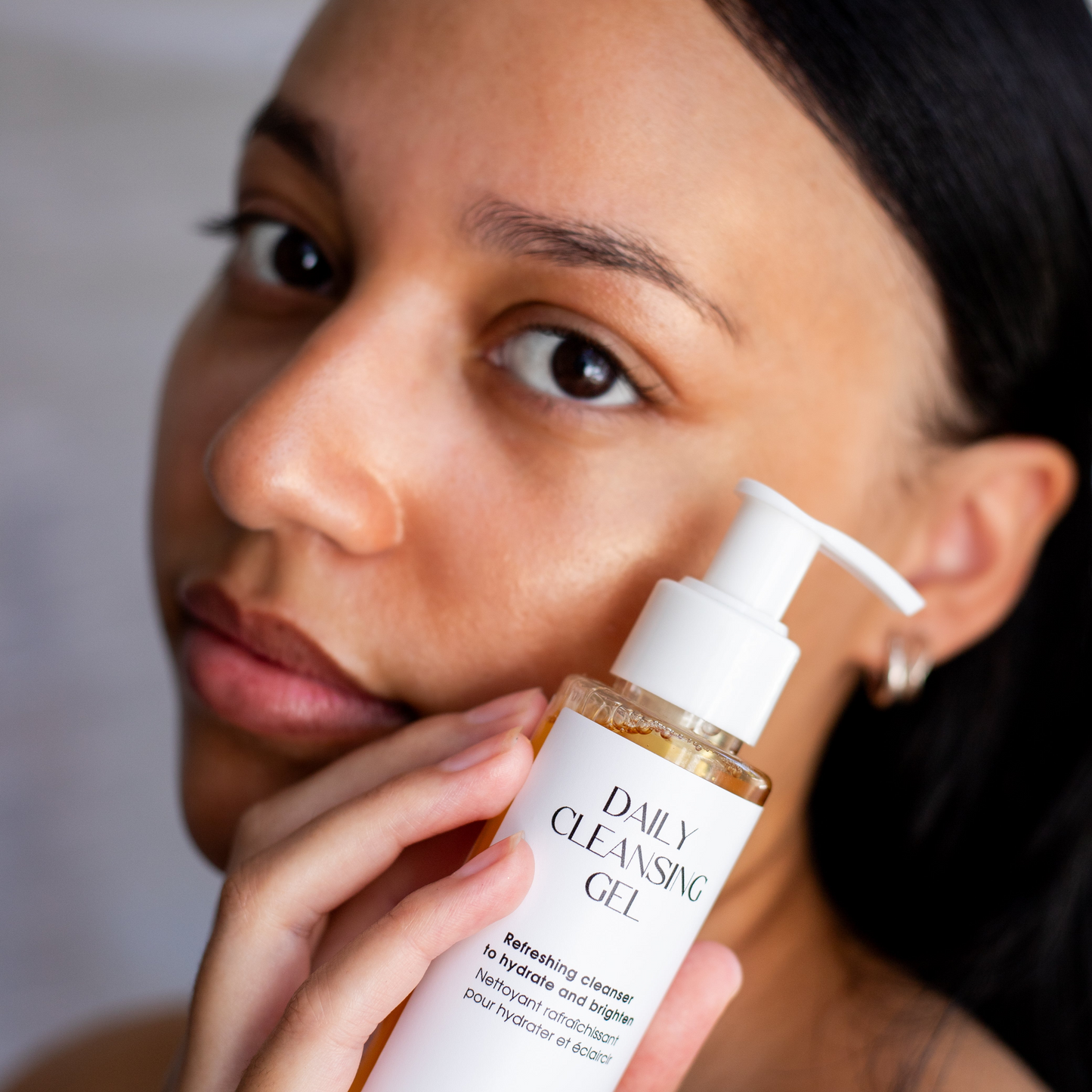 Person holding a bottle of 'Daily Cleansing Gel' with a neutral background