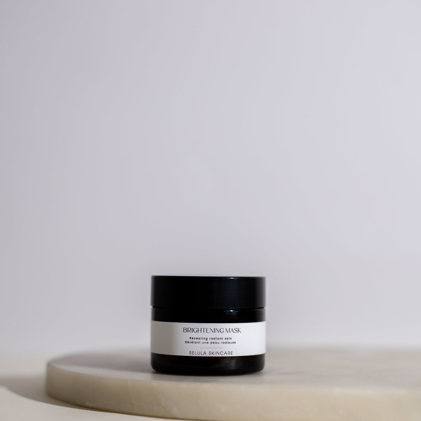 Black jar with white label on a beige surface against a light gray background