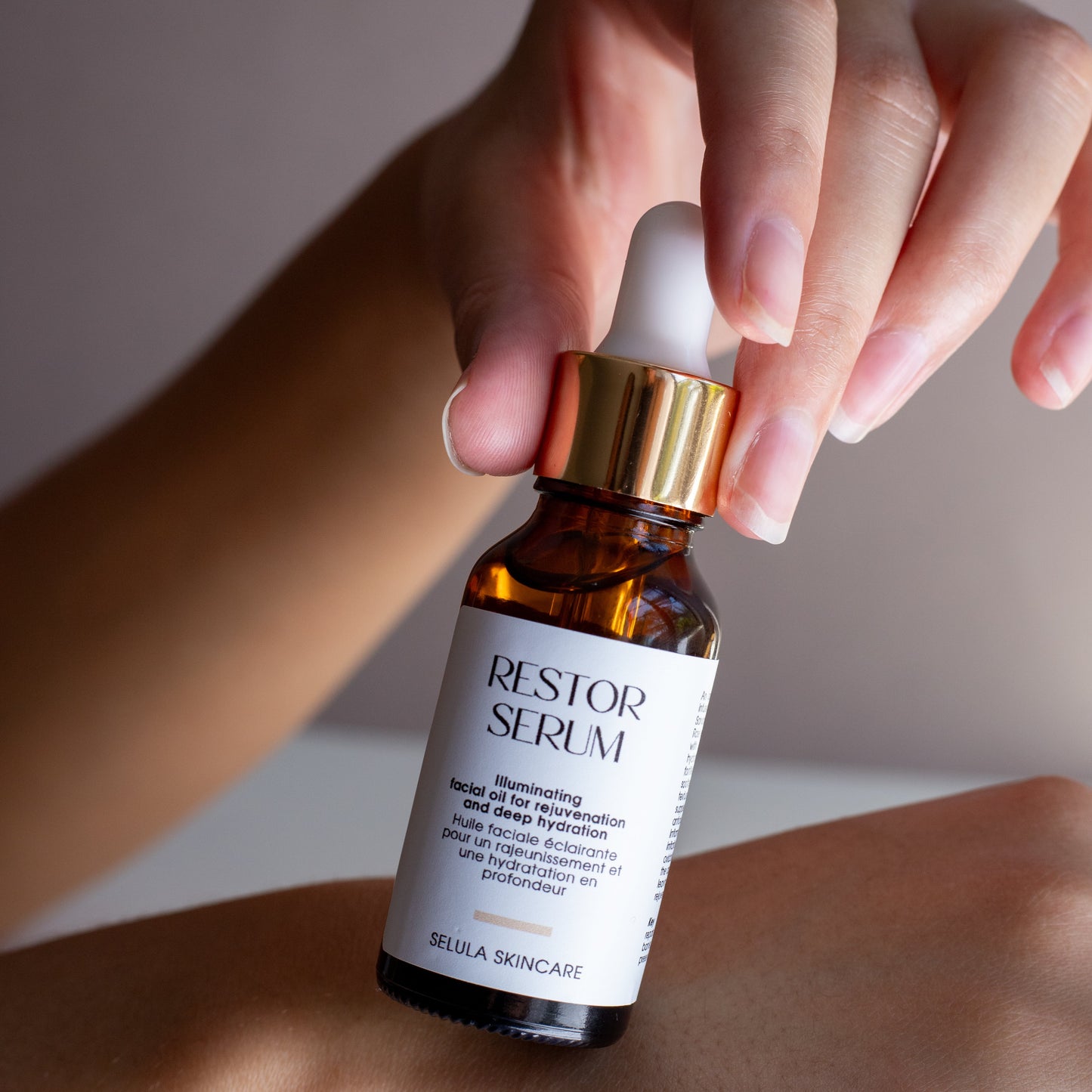 Hand holding a bottle of 'RESTOR Serum' on a neutral background